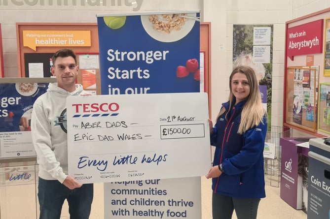  Jon Butler, a director of Aber Dads and Tesco Aberystwyth Community Champion, Chelsey, with a cheque for £1,500